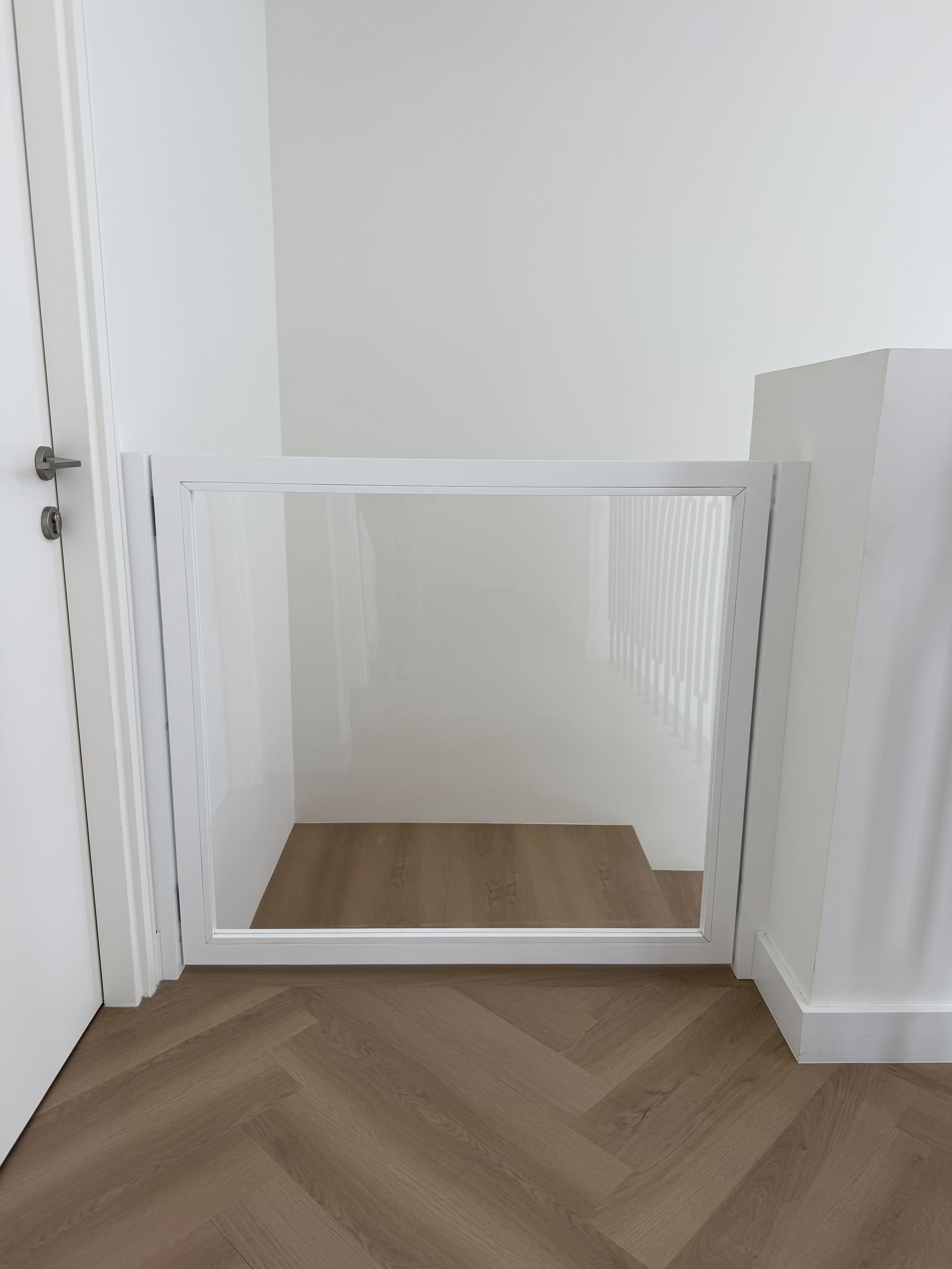 White framed clear safety gate fitted across the stair opening, closed